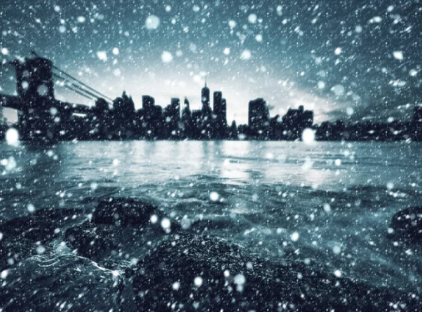模糊的曼哈顿天际线与布鲁克林大桥 降雪期间 东河岸边的岩石和石头 — 图库照片