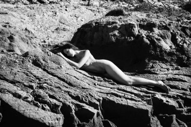 Plajda çıplak kız tans. Genç çıplak kadın bir kumtaşı yalan. Siyah beyaz resim