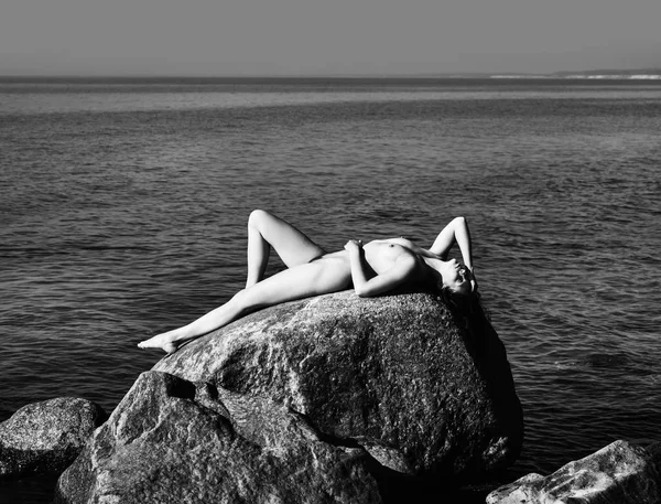Çıplak kız açık havada doğanın keyfini. Güzel genç çıplak kadın denize karşı büyük taşlar üzerinde yatıyor. Vücudunda Çıplaklar Plajı mükemmel çıplak kadınla. Siyah beyaz resim