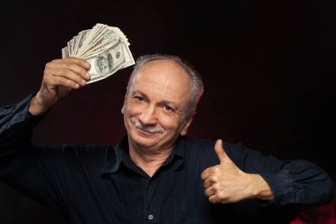 Üst düzey beyefendi tutan bir yığın para. Heyecanlı bir eski işadamı portresi. Mutlu yaşlı adam doları banknot koyu kırmızı zemin üzerine tutarak. 