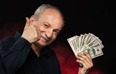 Üst düzey beyefendi tutan bir yığın para. Heyecanlı bir eski işadamı portresi. Mutlu yaşlı adam doları banknot koyu kırmızı zemin üzerine tutarak. 