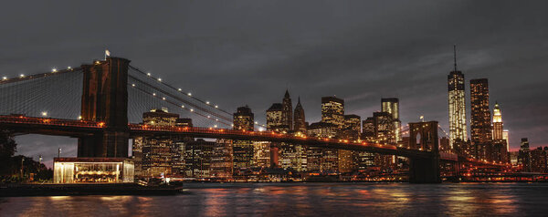 New York City panoramic view of Brooklyn Bridge, East River and Manhattan at sunset with lights and reflections.