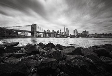 NEW YORK, USA - Apr 29, 2016: Black and white image of Manhattan skyline with Brooklyn Bridge. Rocks and stones on the shore of the East River. Manhattan skyline from Dumbo clipart