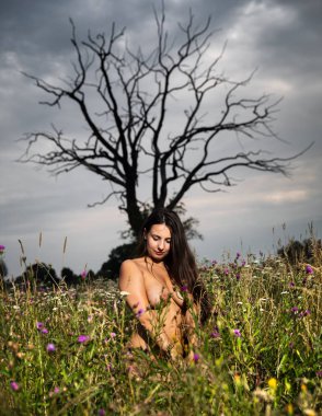 Sağlıklı yaşam ve güzellik kavramı. Çıplak kız açık. Genç çıplak kilolu kadın iri göğüslü yaşlı bir kuru ağaç arka planı bir çayır poz
