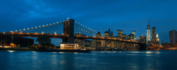 Panorama of Brooklyn Bridge, East River and Manhattan at sunset with lights and reflections. New York, USA