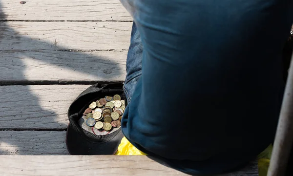 U čepice sedí žebrák s mincemi — Stock fotografie