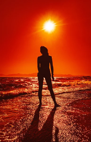 Mujer de pie en una puesta de sol en las olas del océano — Foto de Stock