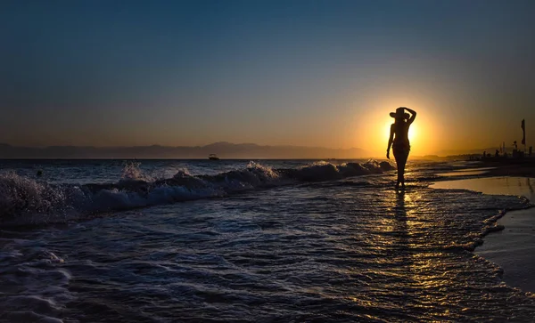 Frau steht auf einem Sonnenuntergang in Meereswellen — Stockfoto