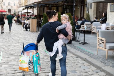 Lviv, Ukrayna - 23 Mayıs 2020: Lviv 'in merkez sokakları ve mimarisi. Koronovirüs enfeksiyonu nedeniyle karantinanın zayıflaması sırasında kollarında küçük bir kızla genç bir anne Lviv sokaklarında