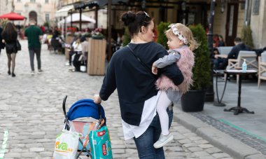 Lviv, Ukrayna - 23 Mayıs 2020: Lviv 'in merkez sokakları ve mimarisi. Koronovirüs enfeksiyonu nedeniyle karantinanın zayıflaması sırasında kollarında küçük bir kızla genç bir anne Lviv sokaklarında