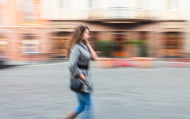 Şehir arka planında arabalı bir cep telefonuyla konuşan genç bir kadının soyut görüntüsü. Kasıtlı hareket bulanıklığı