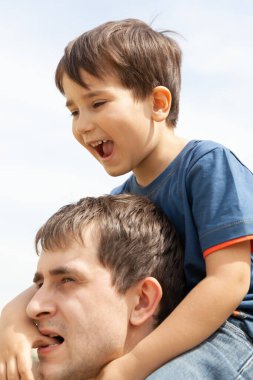 Aile ve mutlu yaşam tarzı kavramı. Çocuk babasının boynunda oturuyor..
