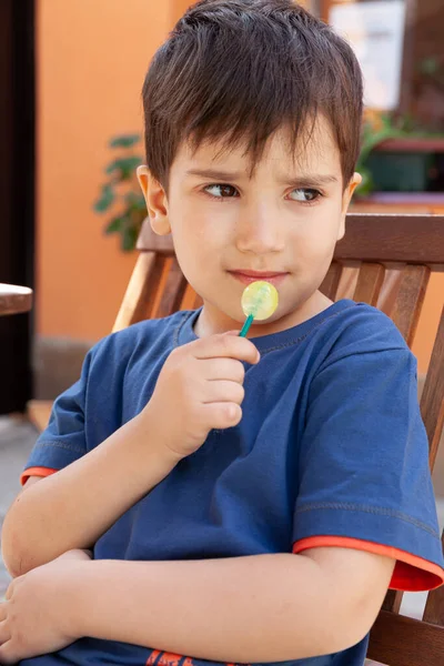 幸せな子供時代のコンセプト かわいい男の子食べるロリポップキャンディーと楽しい屋外を持っている — ストック写真