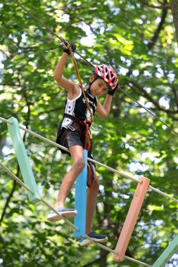 UZHOROD, UKRAINE - 23 Haziran 2020 Macera Parkı 'nda ekstrem spor. Genç bir çocuk ağaçların arasından kablo yolundan geçiyor.