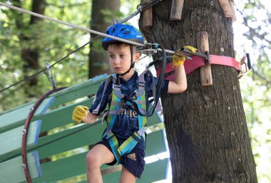 UZHOROD, UKRAINE - 23 Haziran 2020 Macera Parkı 'nda ekstrem spor. Genç bir çocuk ağaçların arasından kablo yolundan geçiyor.