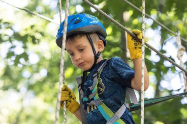 UZHOROD, UKRAINE - 23 Haziran 2020 Macera Parkı 'nda ekstrem spor. Genç bir çocuk ağaçların arasından kablo yolundan geçiyor.