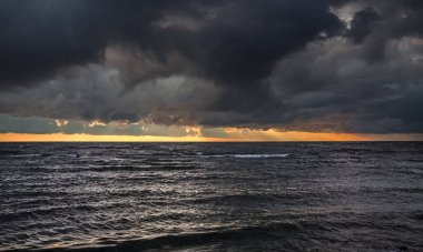 İnanılmaz dramatik manzara. Denizde gün batımında dramatik kara bulutlar. Karanlık deniz suyu ve ağır gri bulutlar..