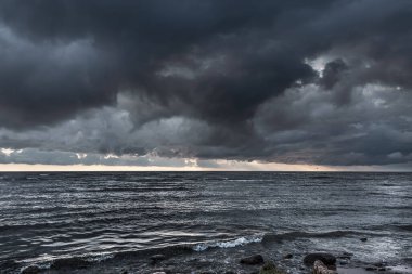 İnanılmaz dramatik manzara. Denizde gün batımında dramatik kara bulutlar. Karanlık deniz suyu ve ağır gri bulutlar..