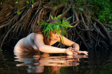 Kafasında eğreltiotu çelengi olan genç ve güzel bir kadın orman nehrinde doğanın tadını çıkarıyor.