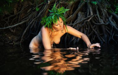 Kafasında eğreltiotu çelengi olan genç ve güzel bir kadın orman nehrinde doğanın tadını çıkarıyor.