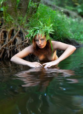 Kafasında eğreltiotu çelengi olan genç ve güzel bir kadın orman nehrinde doğanın tadını çıkarıyor.