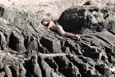 Plajda çıplak kız bronzlaşması. Kumtaşında çıplak genç bir kadın