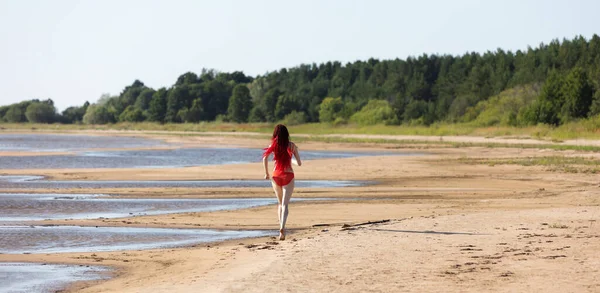 美しい女の子は屋外で自然を楽しむ 赤い水着に緋色のドレッドドレッドロックを持つ若い女性が海に向かって砂に沿って歩く — ストック写真