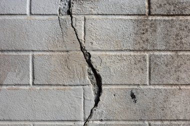 Yıpranmış, gri tuğladan bir duvarın yakın çekimi, ortada belirgin bir dikey çatlak var..