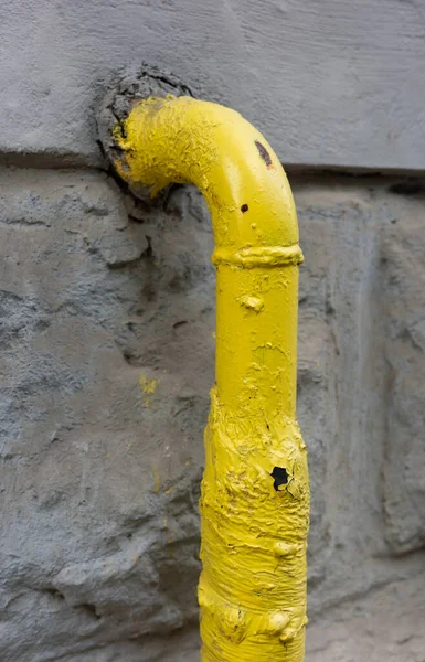 Sarı bir gaz borusunun, eskimiş ve yırtılmış gri bir duvara yakın çekimi..