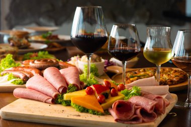 Farklı et, peynir ürünleri ve ahşap tahta üzerinde şarap bardakları ile Antipasti tabağı.