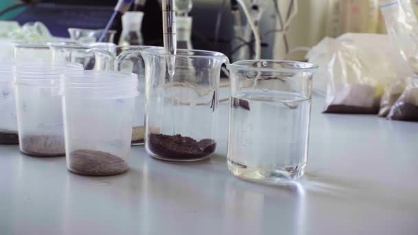 Agua que vierte en vasos de precipitados químicos con el suelo — Vídeos de Stock