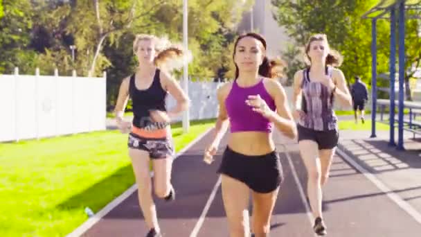 Три молодые женщины бегут на спортивной площадке — стоковое видео