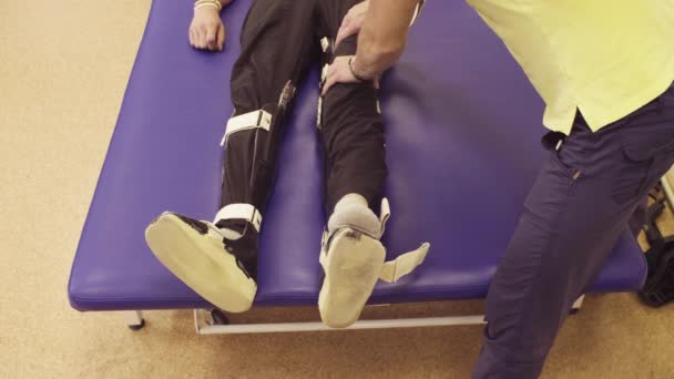 Doctor physiotherapist putting the orthosis for disabled man — Stock Video