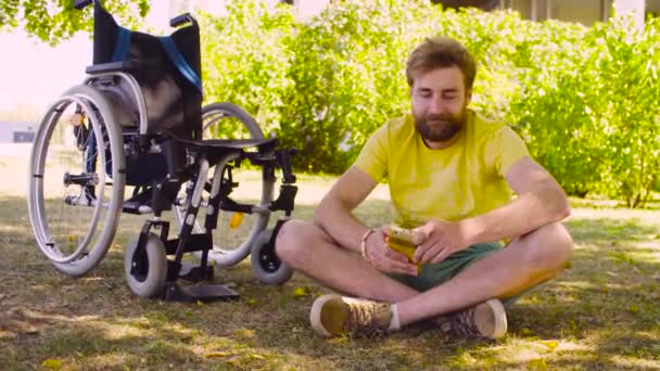 Heureux jeune homme handicapé assis sur l'herbe dans le parc — Video