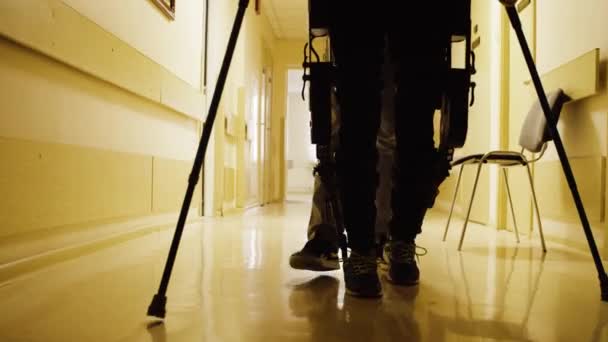 Legs of invalid in robotic exoskeleton walking through the corridor — Stock Video