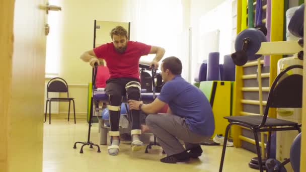 Инвалид в ортезе встает с опорой на две ходунки — стоковое видео