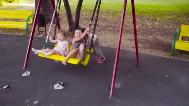 Duas raparigas estão sentadas num baloiço e a terceira está a empurrá-las. — Vídeo de Stock