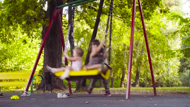 Two girls are sitting on a swing, and the third is pushing them — Stock Video