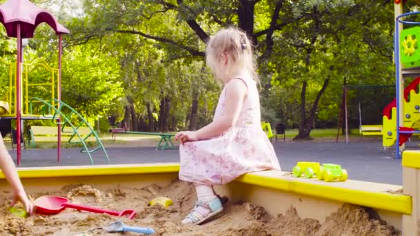 Mała dziewczynka siedzi w piaskownicy jest podniesienie piasku — Wideo stockowe