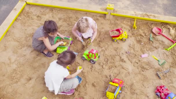 Drie meisjes zitten in een zandbak en oppakken van zand — Stockvideo