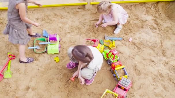 Three girls sitting in a sandbox and picking up sand — Stock Video