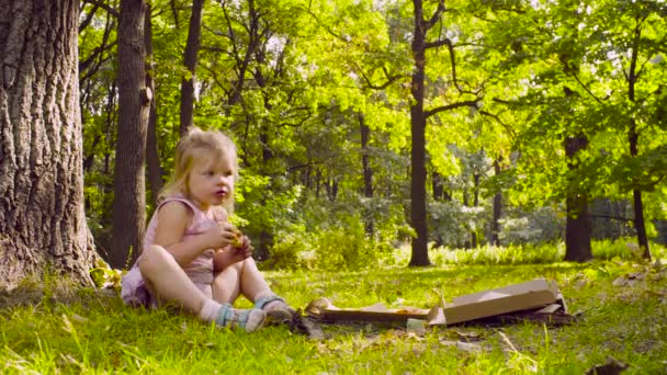 Küçük kız parkta oturan ve pizza yemek — Stok video