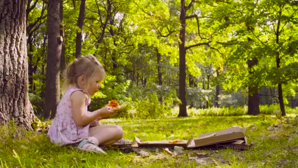 Petite fille assise dans le parc et mangeant de la pizza 
