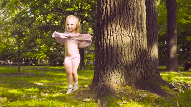 Una niña jugando en un parque en la hierba cerca del árbol — Vídeos de Stock