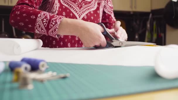 Mãos de mulher de meia-idade com tesoura cortando padrão de papel. Roupas feitas à mão . — Vídeo de Stock