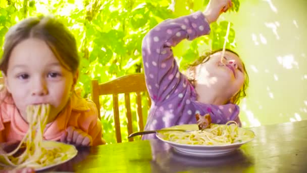 Deux vilaines filles sont assises à la table et mangent des pâtes et des saucisses frites — Video
