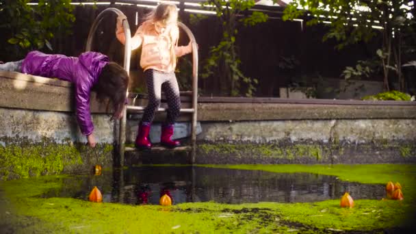 Dos chicas jugando cerca de la vieja piscina cubierta de hierba de pato — Vídeos de Stock