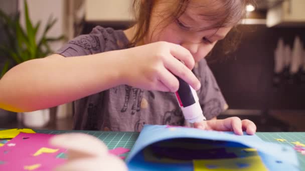 Маленькая девочка склеивает цветную бумагу — стоковое видео