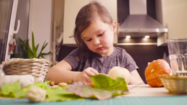 Little girl sitting at the desk makes necklace of acorns — Stock Video