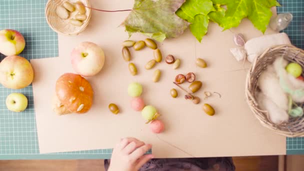 Little girl sitting at the desk makes necklace of acorns — Stock Video